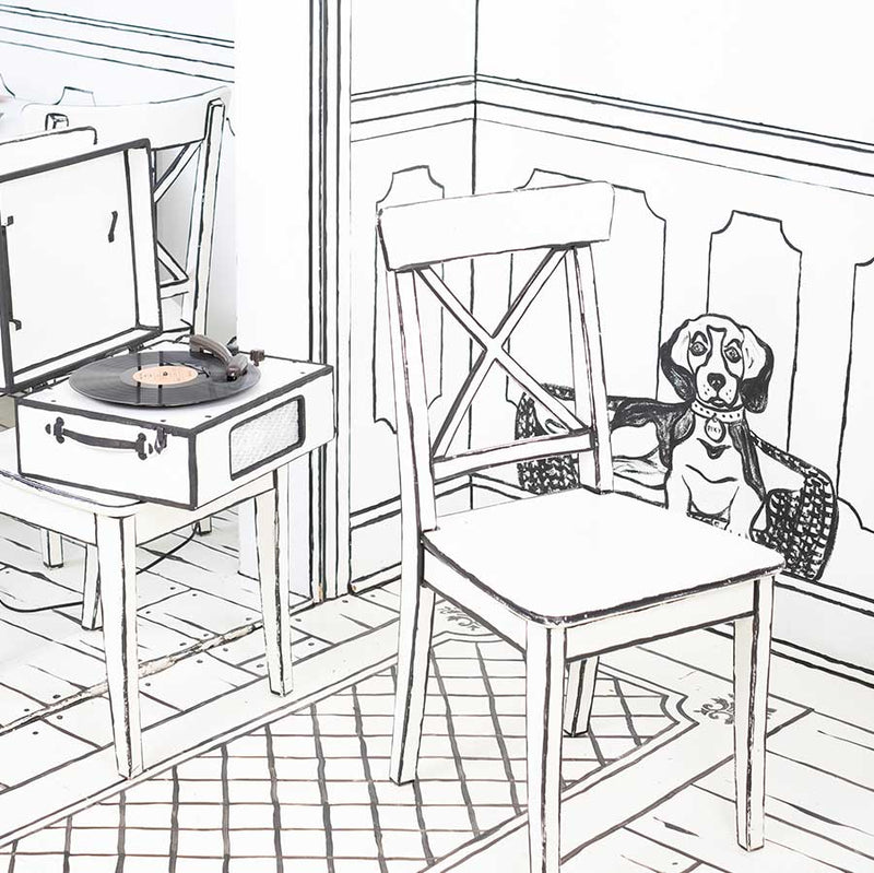 Photo of a black and white illustration room that looks like a colouring book. There is two chairs, one that has a record player on it. Behind the chair is a sketch of a dog.