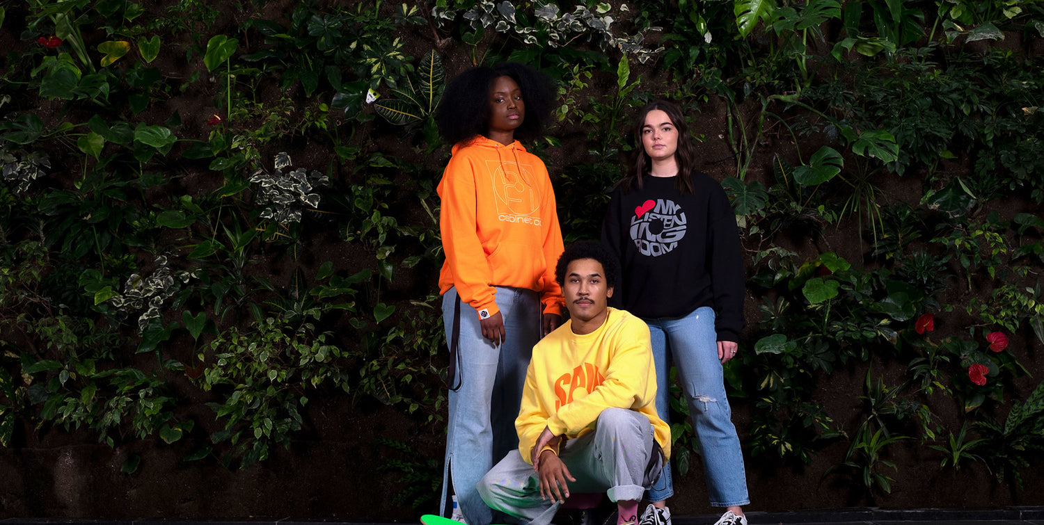 Group photo of three people who are wearing Hifi sweaters and are in front of a greenery wall