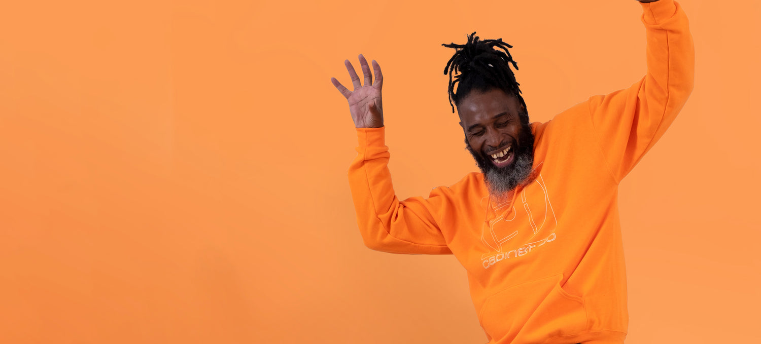 Man on an orange background wearing an orange hoodie with the Hifi cabinet co logo in white on the front of the hoodie