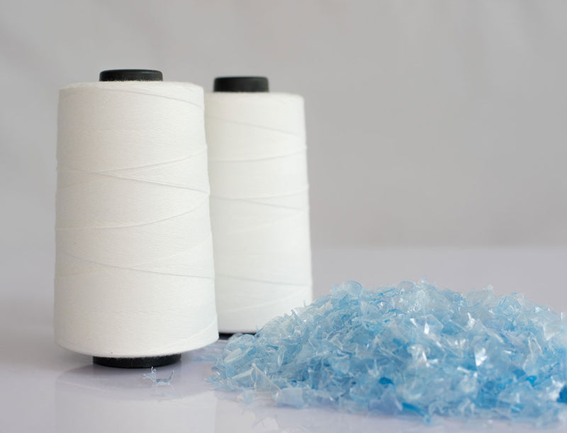 Photo of two rolls of white yarn with a shredded plastic bottle beside it 
