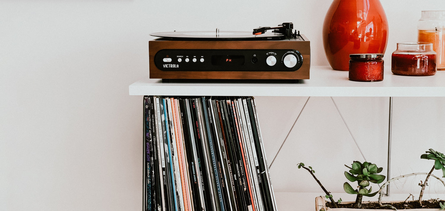 Closeup photo of a whilte shelf holding a record player, records and candles and plants 